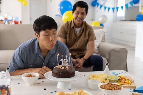 Asian teen blowing out 18th birthday candles with father at home party