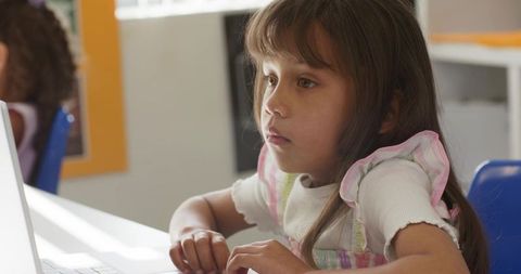 Hispanic girl learning on laptop in classroom close-up with focused thoughtful expression