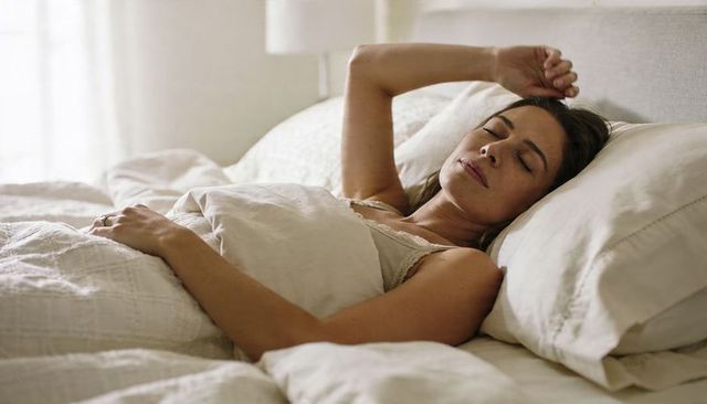 Woman resting peacefully in soft daylight on cozy white bed with linen duvet and pillows
