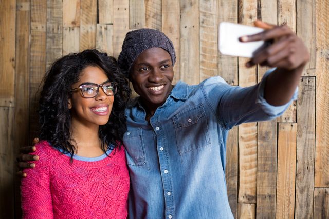 Couple taking a selfie from mobile phone against wooden wall in cafÃ©