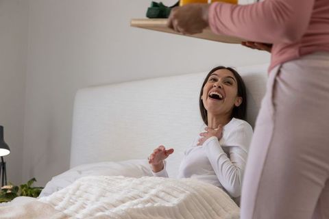 Female couple sharing breakfast in bed laughing and enjoying cozy intimate morning together
