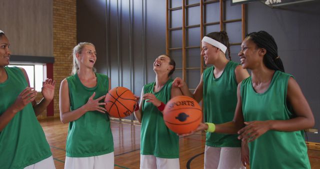 Portrait of diverse female basketball team laughing and holding balls. basketball, sports training at an indoor court.