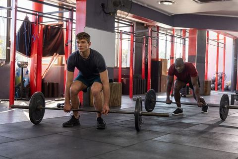 Diverse male training partners preparing deadlifts with loaded barbells in CrossFit gym