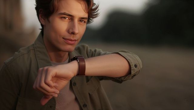 Young man showing leather watch on wrist during golden hour outdoor portrait olive shirt