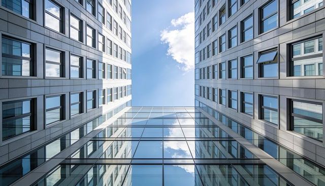 Framing sky through symmetrical glass atrium between modern office towers reflecting clouds