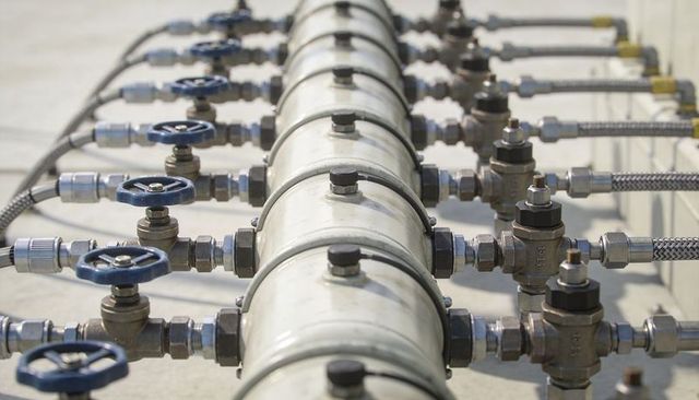 Manifold distributing fluid with blue handwheels and stainless braided hoses on pipeline