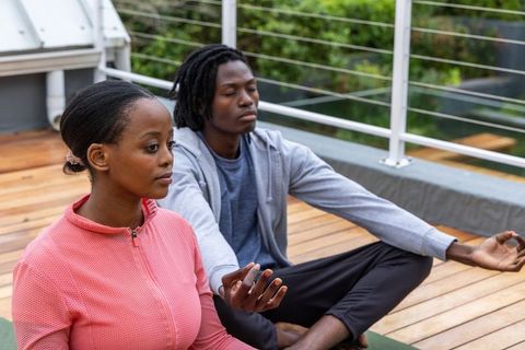 African american couple meditating on rooftop deck practicing mindfulness and yoga