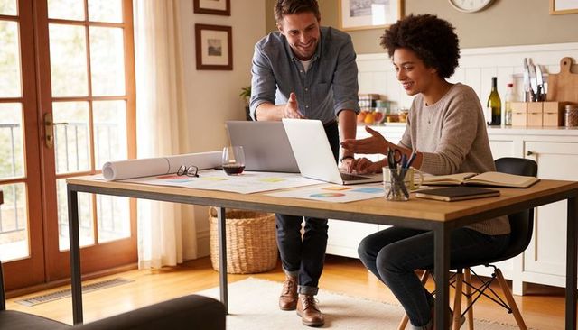 Couple collaborating on laptop in bright home office with charts, plans and coffee