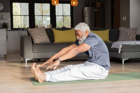 Senior african american man stretching on yoga mat at home for mobility and wellness