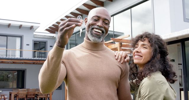 Portrait of happy biracial couple embracing and holding keys at new house. Domestic life, moving house and lifestyle, unaltered.