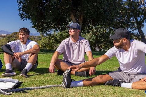 Athletes stretching on park grass before training reaching for cleat near heavy rope