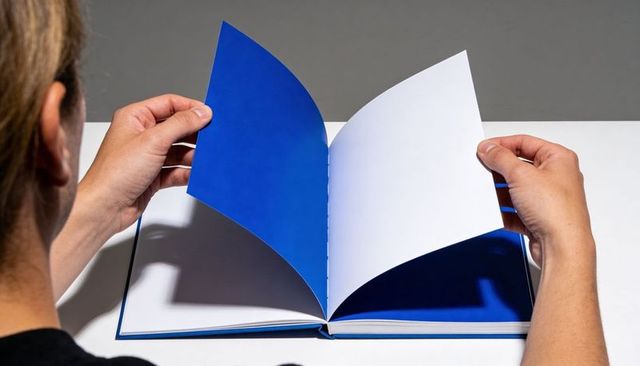 Woman turning blue page in hardcover book with dramatic studio lighting and sharp shadows