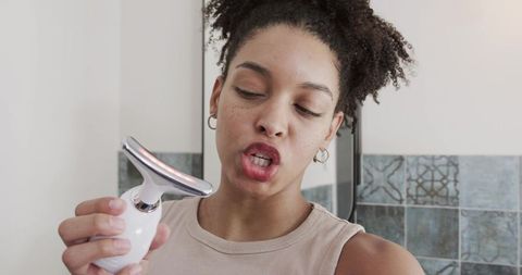 African american woman demonstrating facial massager in bathroom mirror for skincare routine