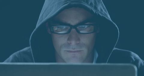 Focused Man in Hoodie Using Laptop in Dark Room
