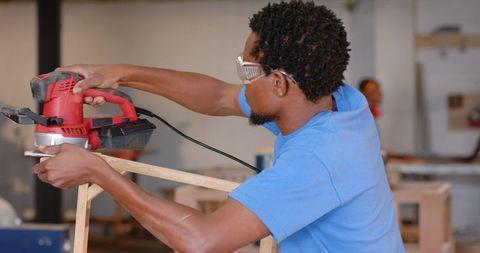 Skilled craftsman using electric sander in woodshop