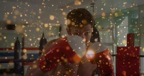 Shirtless boxer raising guard in ring training with red gloves and golden bokeh