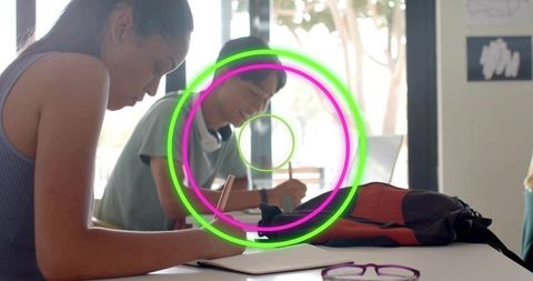 High school students writing and concentrating at bright desk with neon circle overlay