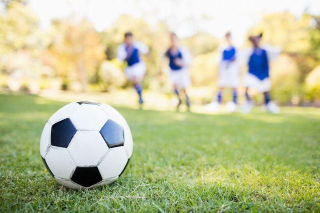Close-up view of a soccer ball on grass with children playing in the background. Ideal for use in sports-related content, youth activities promotions, outdoor recreation advertisements, and team-building visuals.