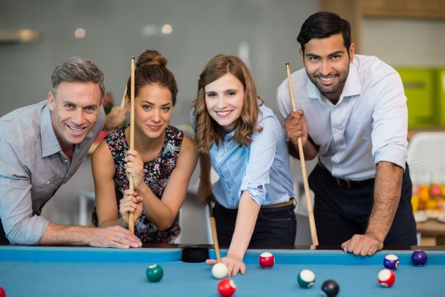 Portrait of smiling business colleagues playing pool in office space