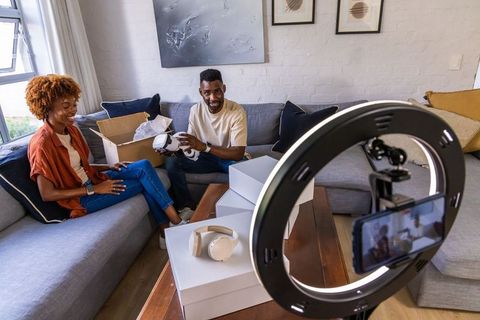African american couple unboxing headphones on sofa recording with ring light tech vlog