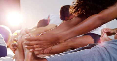Group reaching forward for seated hamstring stretch with backlit warm sun flare