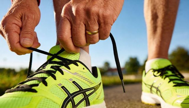 Male runner tying neon yellow running shoes with black laces close-up on paved morning path