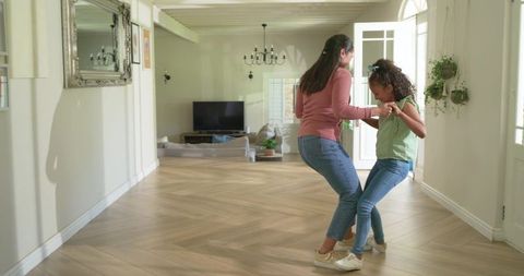 Mother and daughter dancing in sunlit hallway on parquet floor holding hands near door