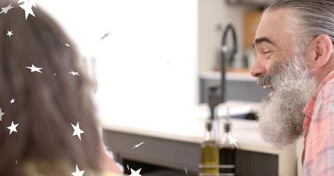 Smiling bearded grandfather chatting with woman in bright cozy kitchen, candid family moment