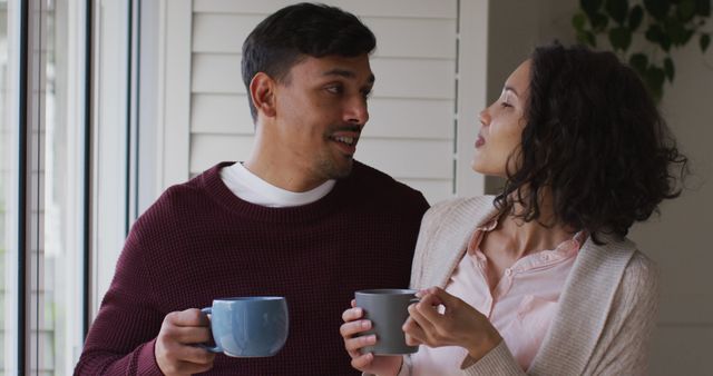 Romantic hispanic couple embracing standing in window having coffee. at home in isolation during quarantine lockdown