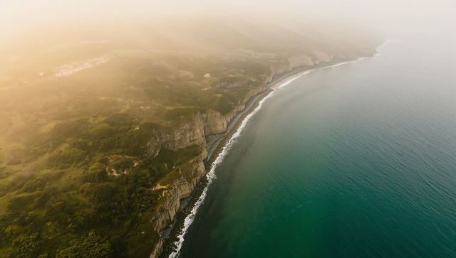 Golden mist over layered cliffs stretching along rugged coastal bluff aerial seascape