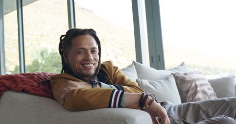 Mid-adult african american man relaxing on gray sofa with textured cushions and bracelets