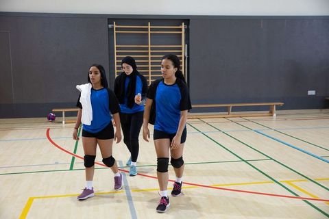 Female volleyball players walking off court after indoor practice wearing team knee pads