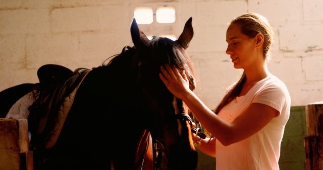 Young woman displaying affection by petting a horse inside a stable. Great for showcasing human-animal bonding, equestrian activities, pet care, animal behavior, and lifestyle contents.
