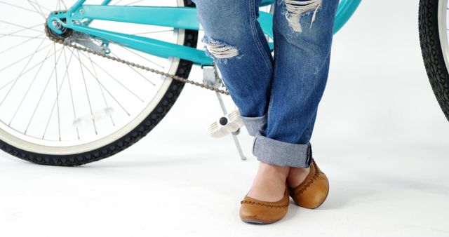 Legs section of caucasian woman in denim trousers with blue bike on white background with copy space. Eco travel, fashion, summer and lifestyle concept, unaltered.