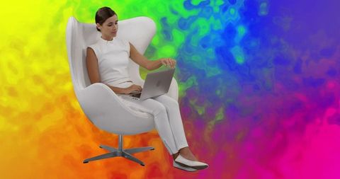 Woman in white clothing using laptop in futuristic chair on vivid background