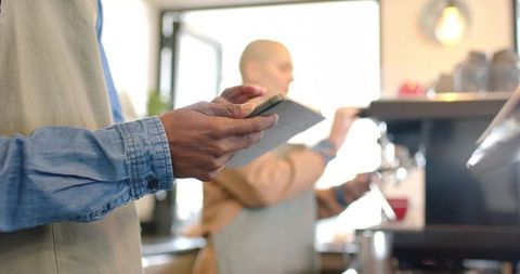 Diverse baristas preparing espresso while recording orders on pad in bright cafe