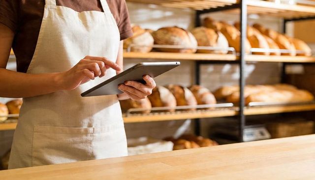 Artisan Baker Checking Tablet at Rustic Bakery Counter with Fresh Loaves