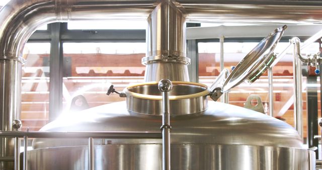 Stainless steel brewing equipment in a modern brewery showing fermentation tank and pipes, useful for illustrating beer production, industrial brewery setups, and the brewing process. Ideal for articles about brewing technology, craft beer industry insights, and promotional materials for brewery tours.