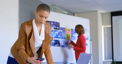 Businesswoman Using Smartphone in Modern Office Setting with Coworker - Download Free Stock Images Pikwizard.com