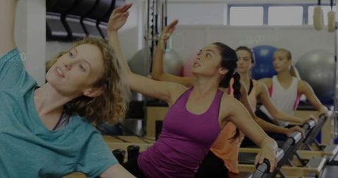 Women reaching on pilates reformers in group class building balance flexibility focus and teamwork