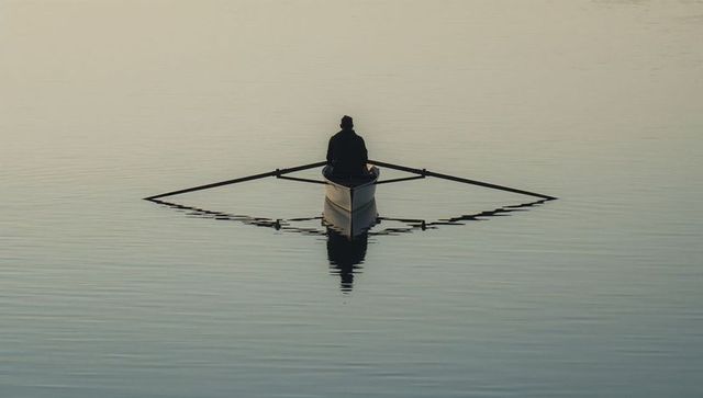Solitary rower gliding on glassy lake at dawn with symmetrical reflection and calm