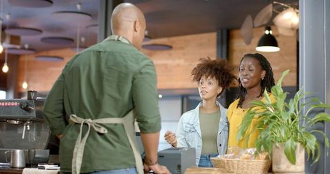 Two african american women ordering coffee from barista at cozy wood-accented café counter