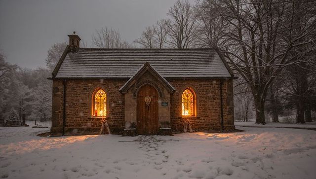 Snowy stone chapel glowing through stained glass at dusk with footprints in churchyard