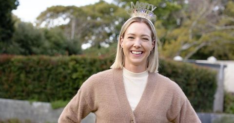 Mid adult woman smiling in backyard wearing merry headband and cozy cardigan lifestyle