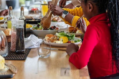 African American Family Sharing Dinner and Serving Fresh Salad Around Wooden Table at Home