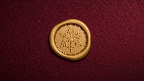 Gold wax seal featuring snowflake on burgundy cardstock for holiday invitation and branding