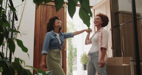 Celebrating new home arrival with friends holding hands in bright foyer with moving boxes