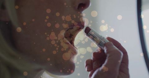 Mature woman applying lipstick at vanity mirror close-up with soft bokeh lighting