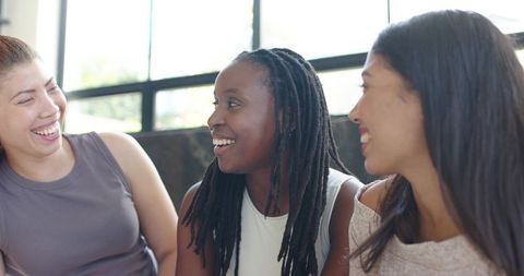 Three women laughing and talking on lounge bench by sunlit window