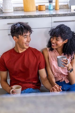 Young diverse couple sharing morning coffee and holding hands on kitchen floor, smiling warmly